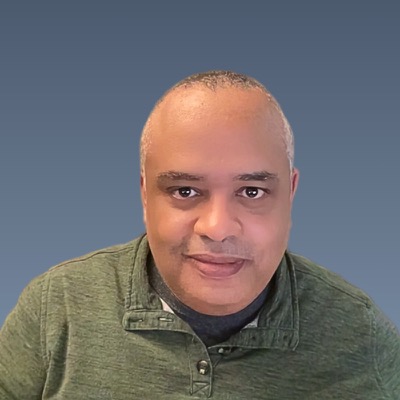Balding man with friendly smile wearing green collared shirt against gray background.