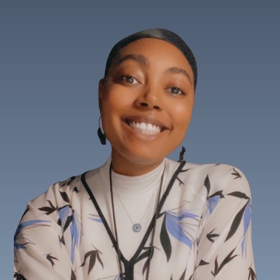 Smiling woman with short hair wearing floral print jacket against blue-gray background.
