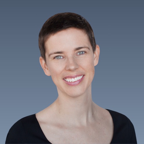 Smiling woman with short dark hair and blue eyes wearing black top against blue-gray background.