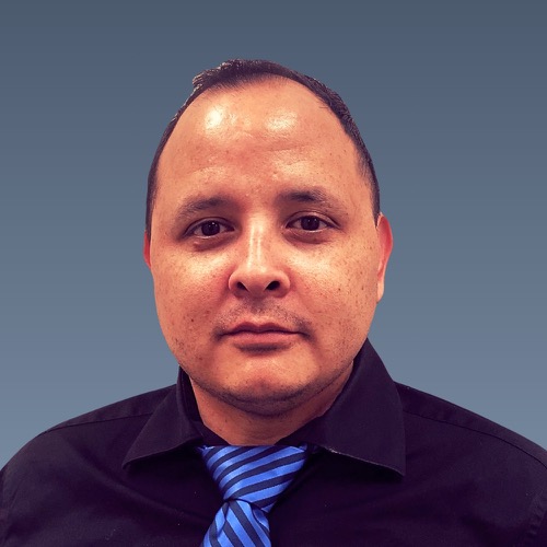 Middle-aged man with short dark hair wearing a dark shirt and blue striped tie against a gray background.