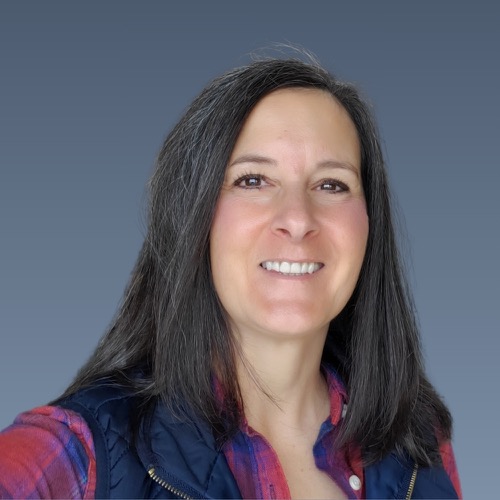 Smiling woman with dark hair wearing white collared shirt against blue background.